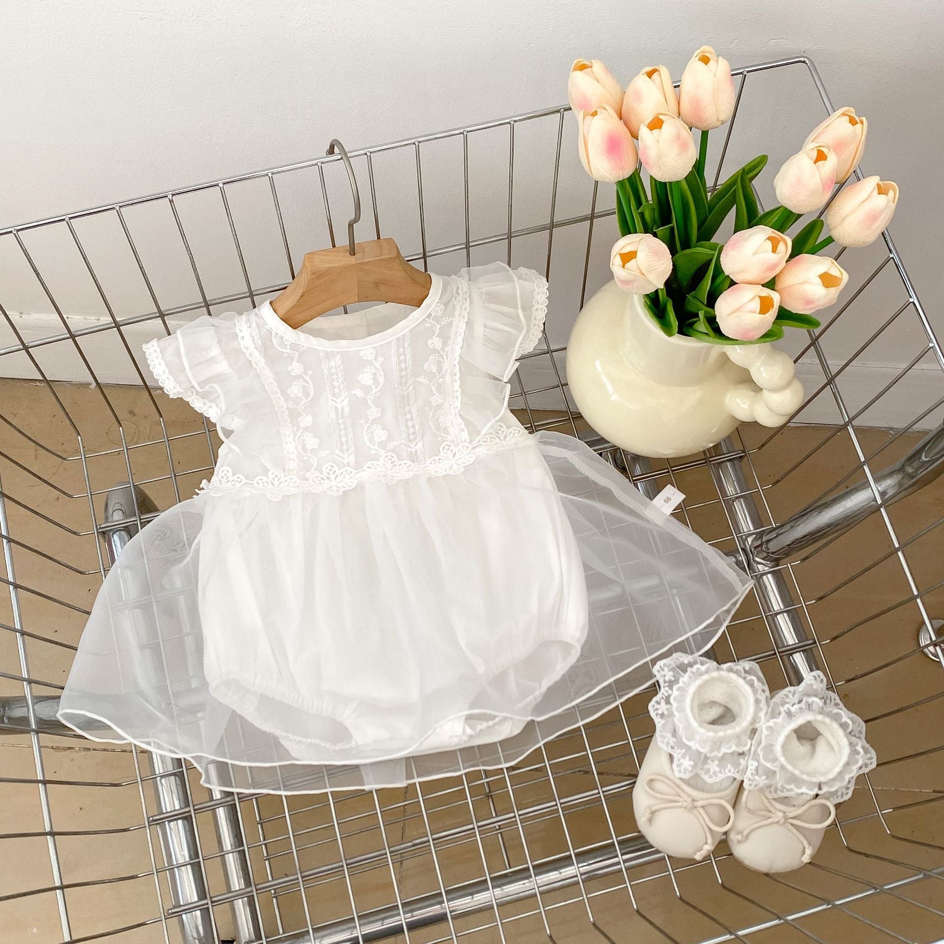 A cute baby girl wearing a white flower-embroidered crew neck top with fly sleeves, perfect for summer.