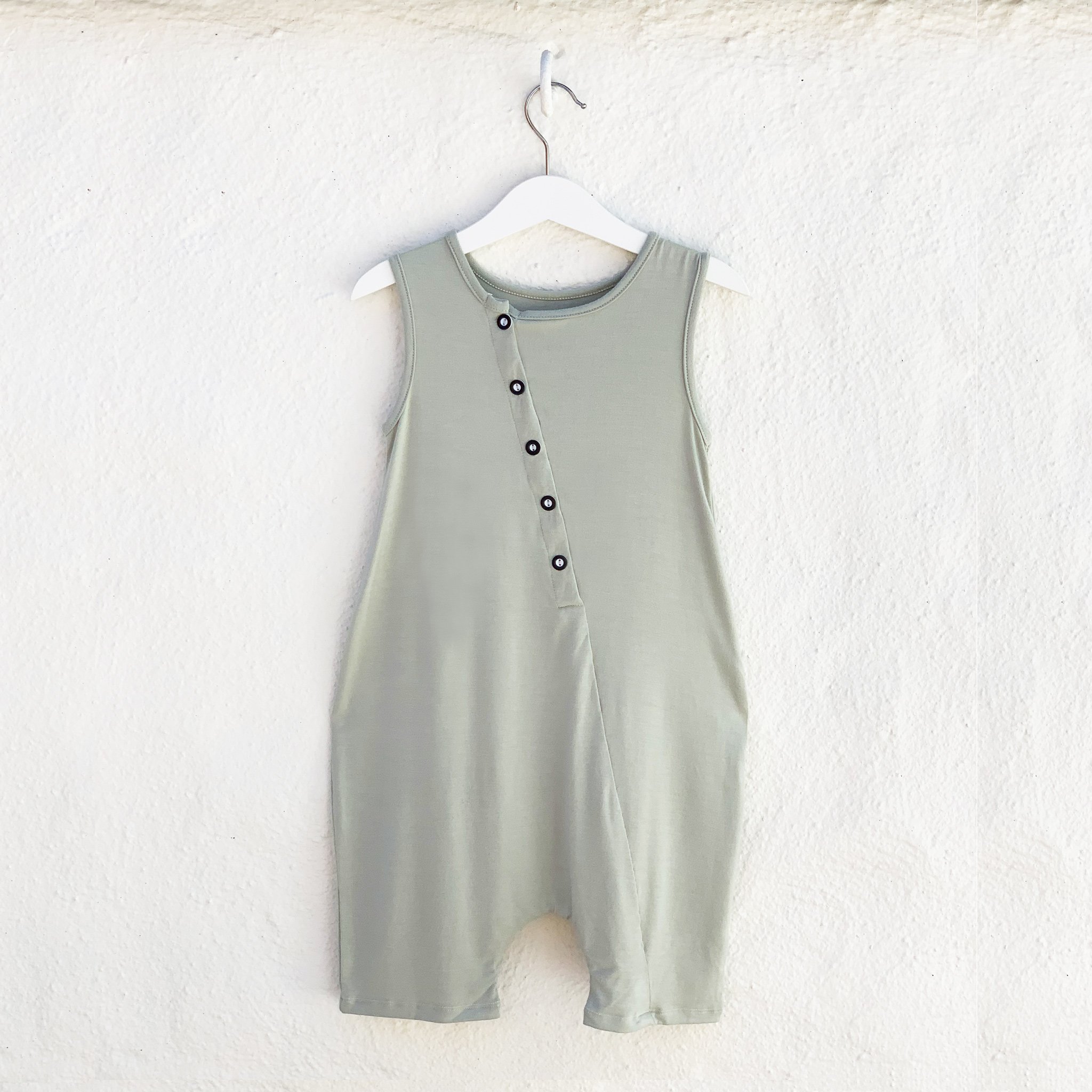 A stylish unisex tank romper in desert sage color, featuring front buttons and a drop crotch design, made from soft rayon and spandex fabric.