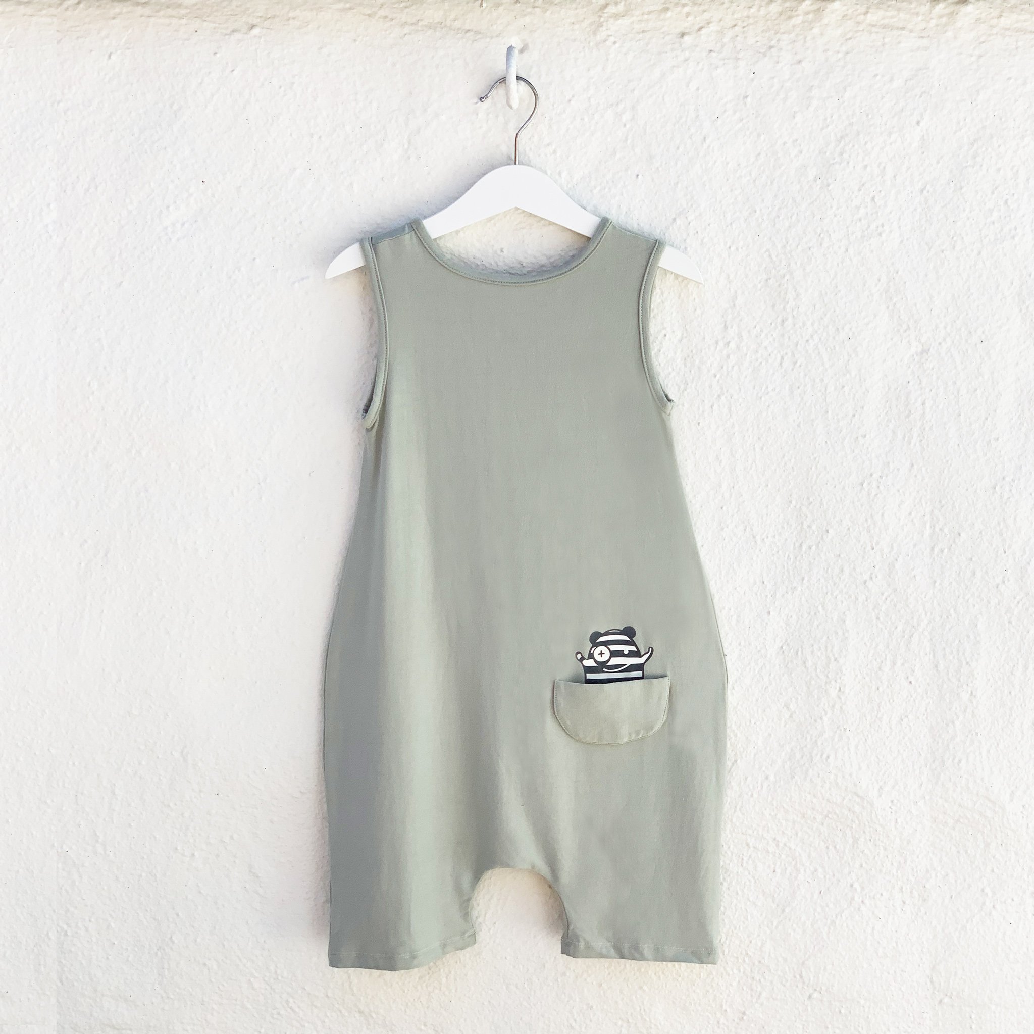 A stylish unisex tank romper in desert sage color, featuring front buttons and a drop crotch design, made from soft rayon and spandex fabric.