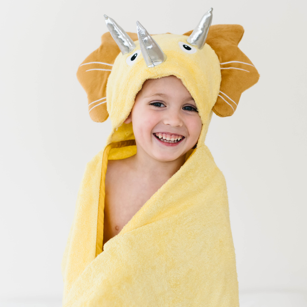 A soft yellow dinosaur hooded towel designed for toddlers, featuring 3D shiny silver horns and velvety frills, perfect for bath time.