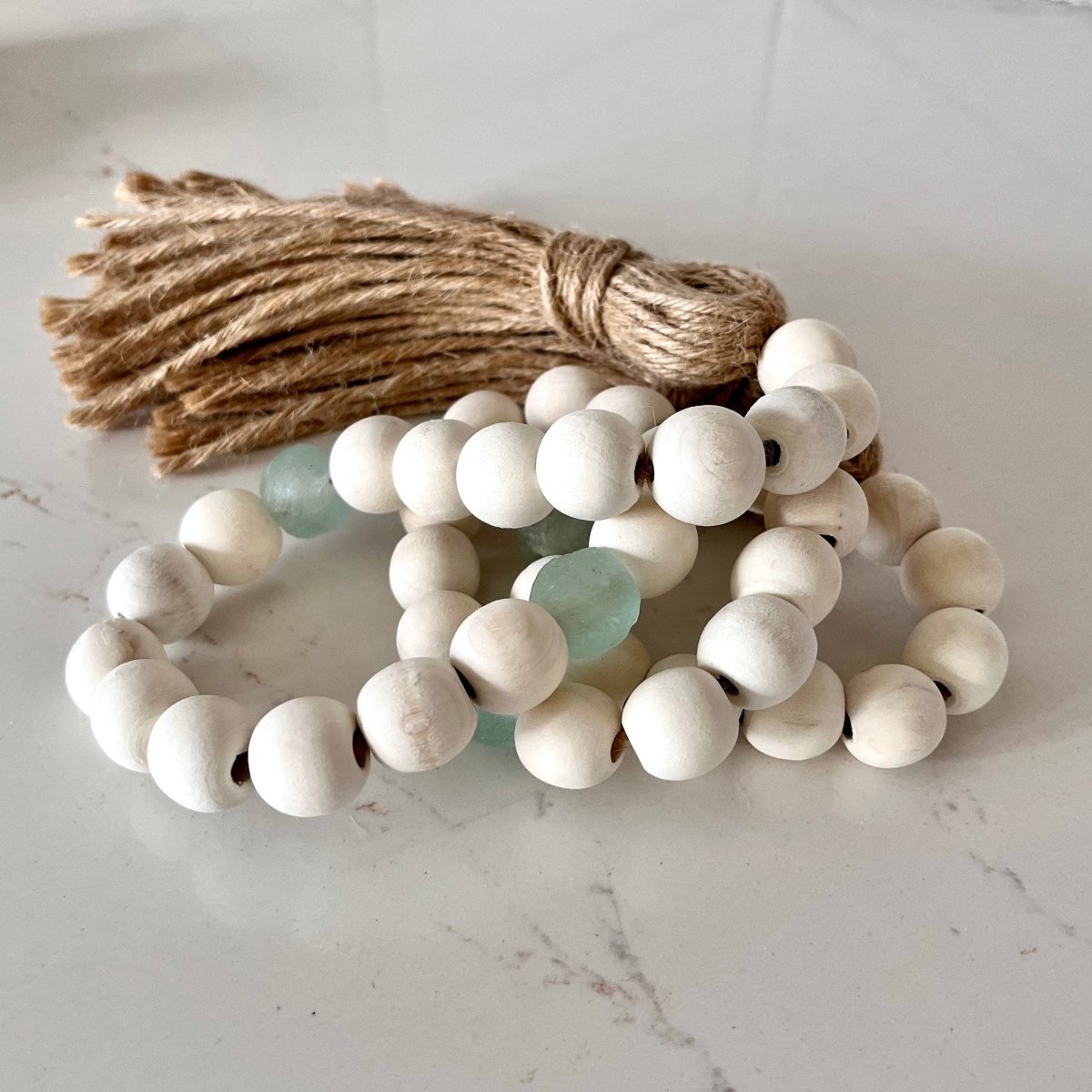 A beautiful whitewashed wood bead garland featuring aqua recycled glass beads and jute tassels, perfect for coastal decor.