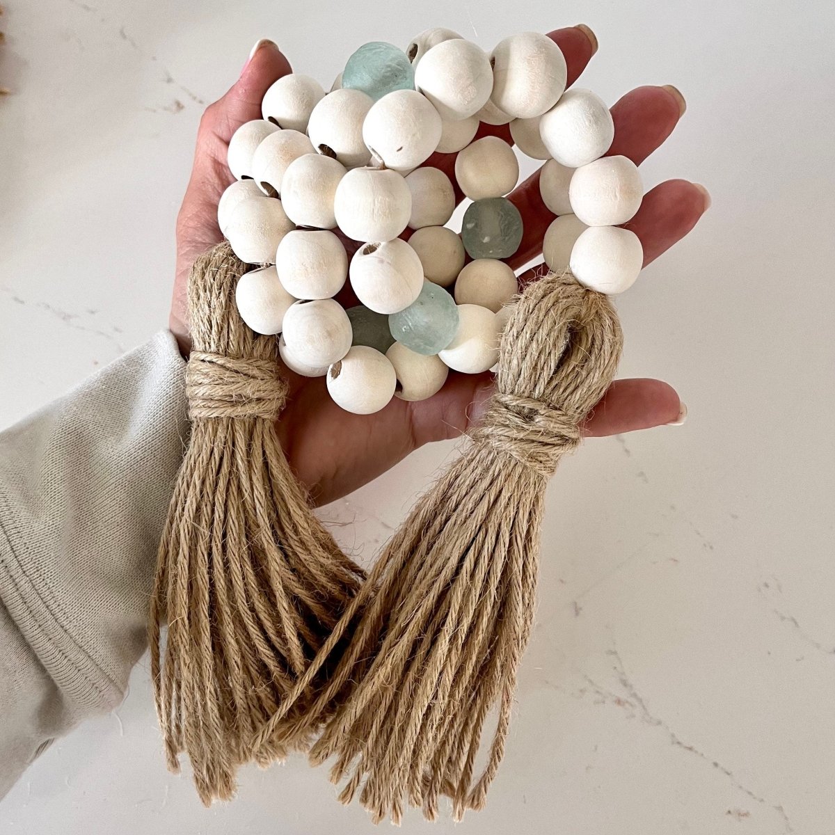 A beautiful whitewashed wood bead garland featuring aqua recycled glass beads and jute tassels, perfect for coastal decor.