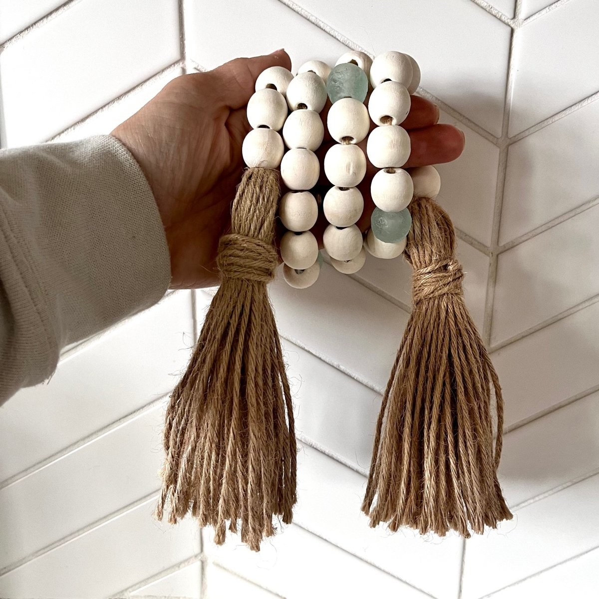 A beautiful whitewashed wood bead garland featuring aqua recycled glass beads and jute tassels, perfect for coastal decor.