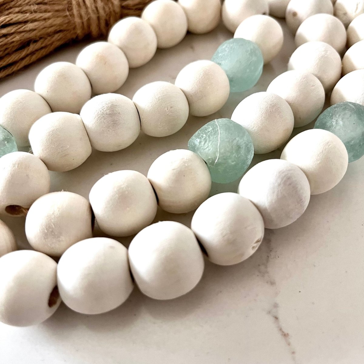 A beautiful whitewashed wood bead garland featuring aqua recycled glass beads and jute tassels, perfect for coastal decor.