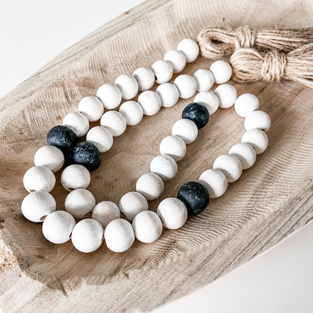 A beautifully crafted Whitewashed Wood Bead Garland featuring Jumbo Black Recycled Glass Beads and jute tassels, perfect for coastal decor.