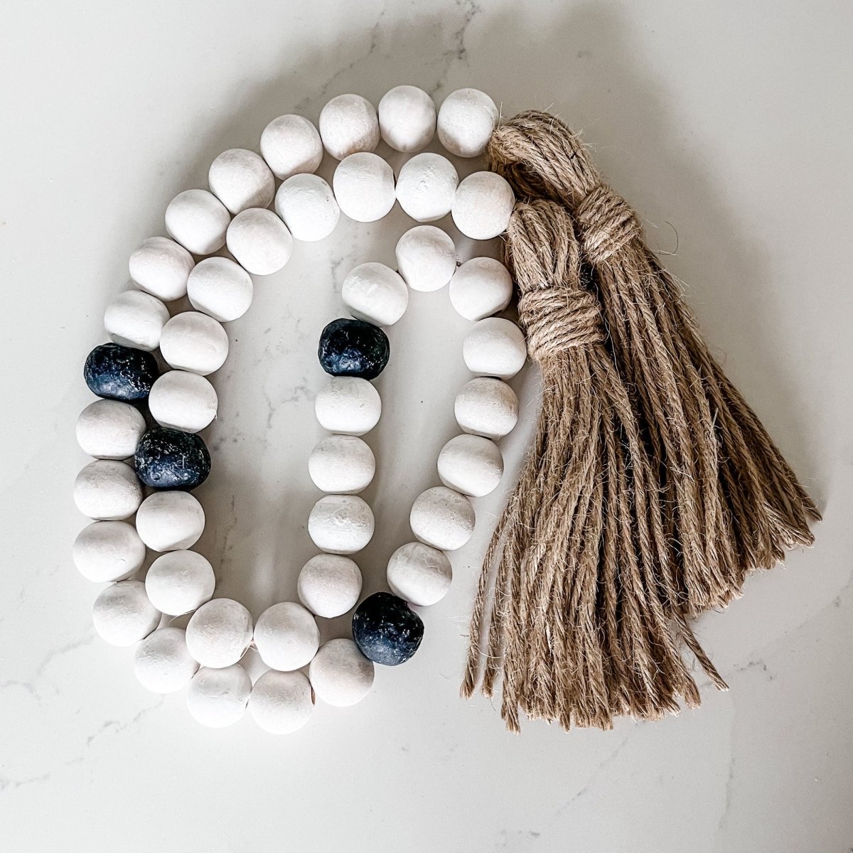 A beautifully crafted Whitewashed Wood Bead Garland featuring Jumbo Black Recycled Glass Beads and jute tassels, perfect for coastal decor.