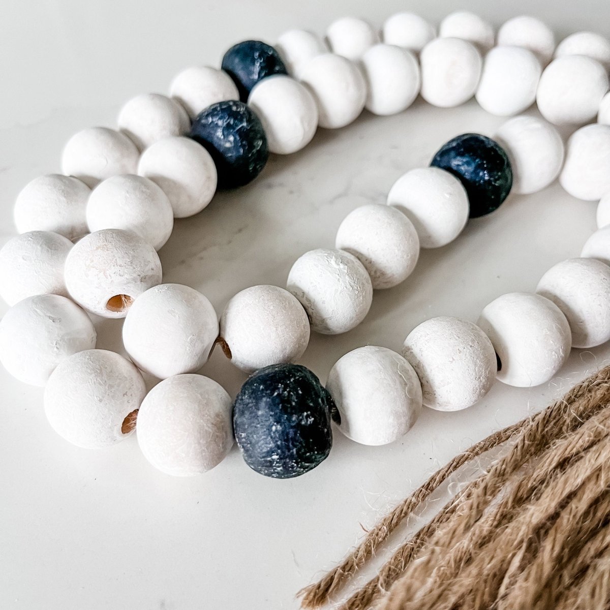 A beautifully crafted Whitewashed Wood Bead Garland featuring Jumbo Black Recycled Glass Beads and jute tassels, perfect for coastal decor.