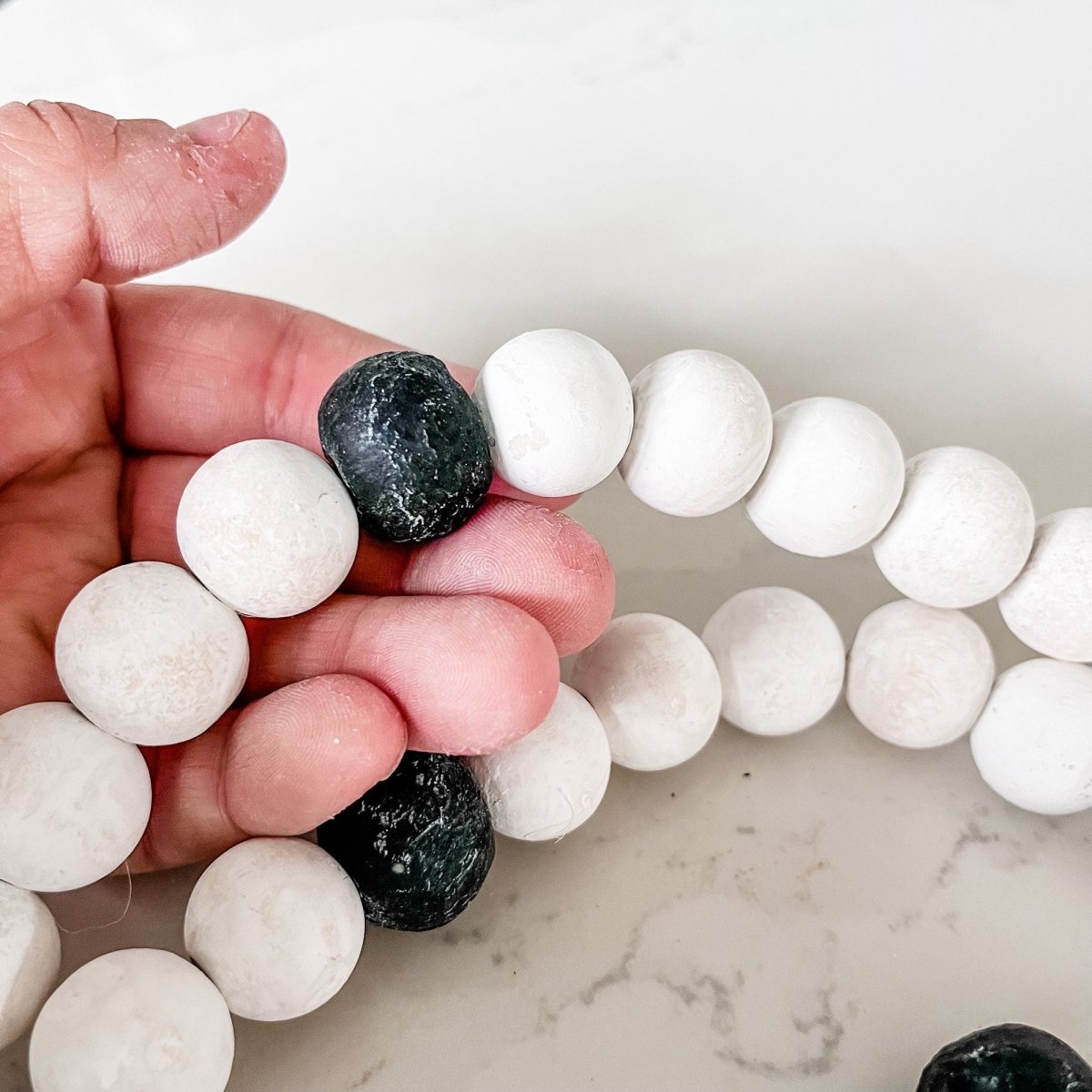 A beautifully crafted Whitewashed Wood Bead Garland featuring Jumbo Black Recycled Glass Beads and jute tassels, perfect for coastal decor.