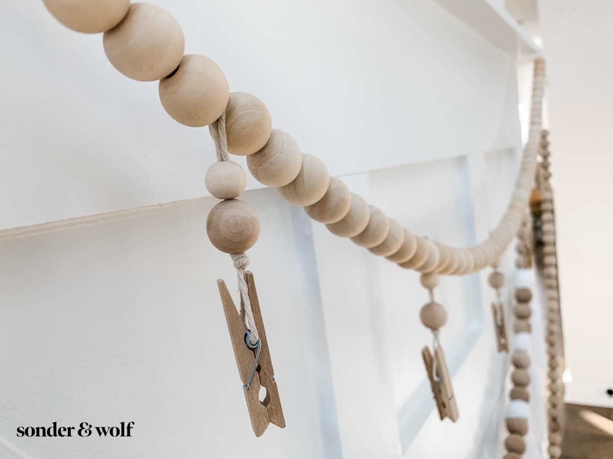 Wood Bead Garland featuring clothespins for hanging photos and masks, showcasing light unfinished wood beads and decorative loops.