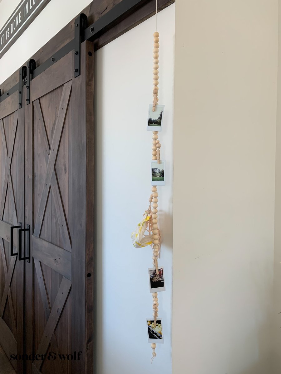 Wood Bead Garland featuring clothespins for hanging photos and masks, showcasing light unfinished wood beads and decorative loops.