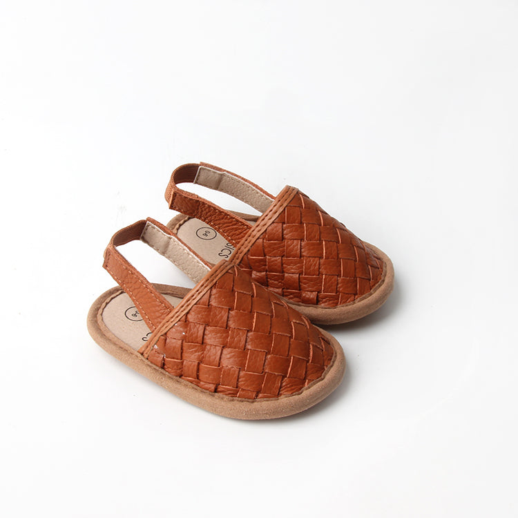 A pair of stylish woven leather sandals in Tawny and Latte colors, designed for toddlers with soft soles and ankle strap buckles.