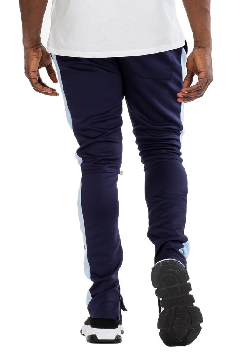 A pair of black skinny fit track pants featuring a single stripe detail, tug-free zipper closure, and hidden ankle zipper, displayed on a model.