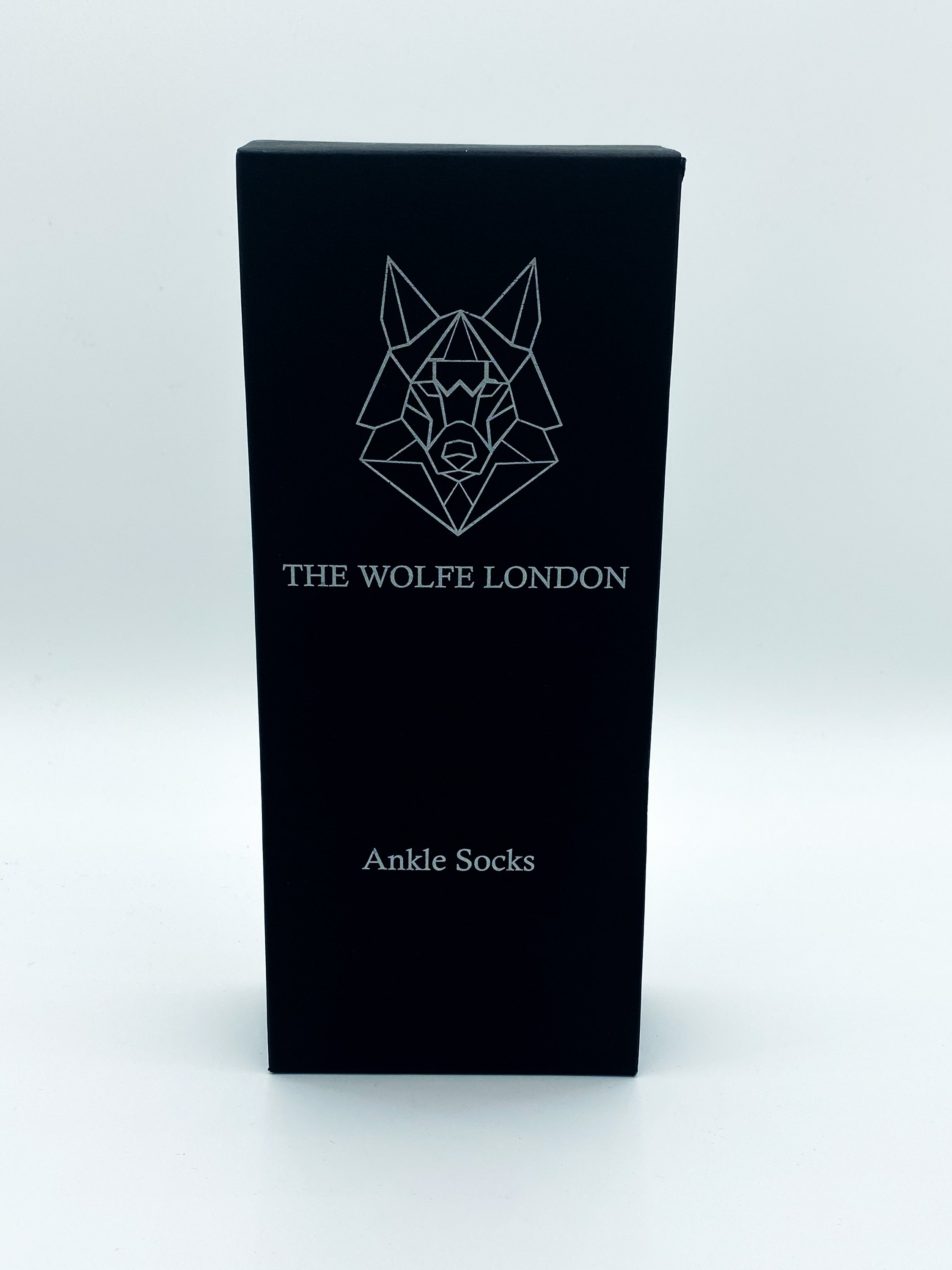 A pair of Alpha Black Ankle Socks featuring a double-tab silhouette, soft black fabric, and white Wolfe logo embroidery on the back.