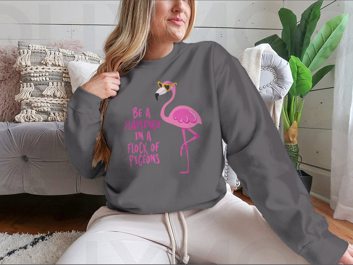 A stylish t-shirt featuring the motivational quote 'Be A Flamingo In A Flock Of Pigeons' in vibrant colors, made from high-quality cotton.