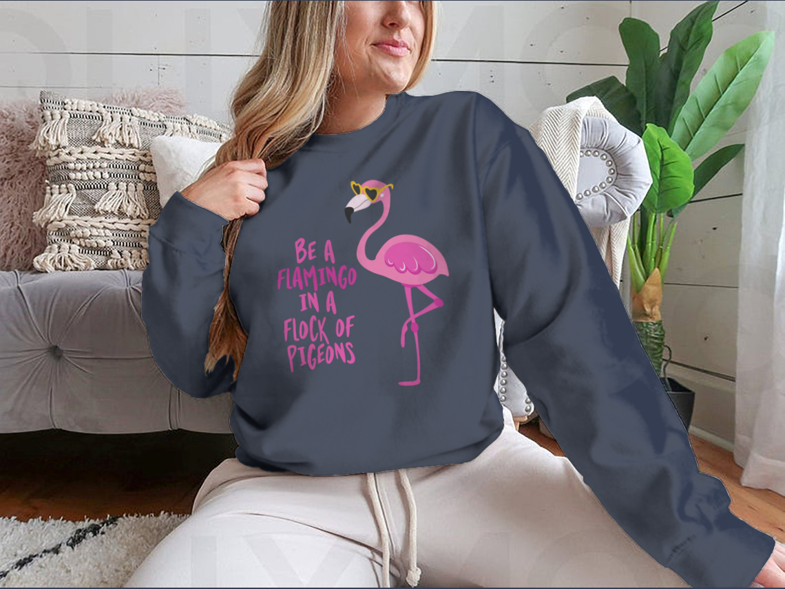 A stylish t-shirt featuring the motivational quote 'Be A Flamingo In A Flock Of Pigeons' in vibrant colors, made from high-quality cotton.