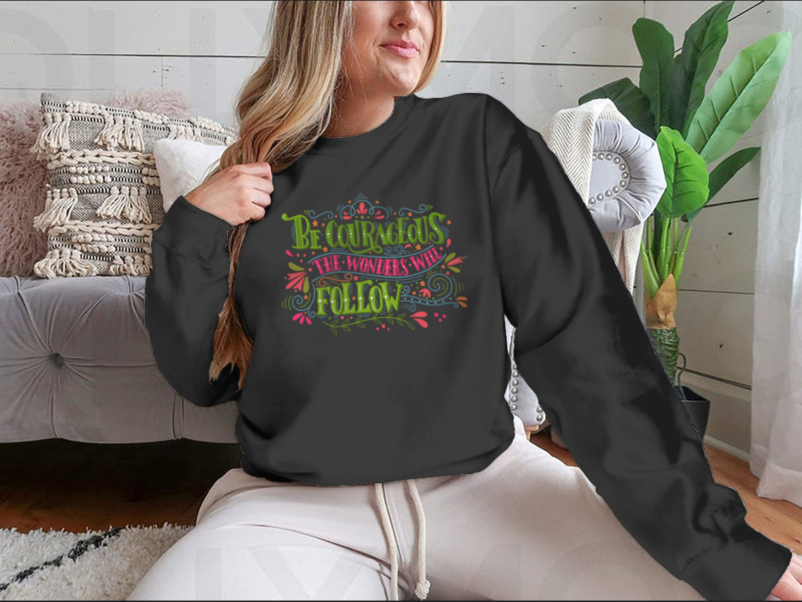 A motivational apparel piece featuring the phrase 'Be Courageous, The Wonders Will Follow' in a stylish design, made from a soft cotton/polyester blend.