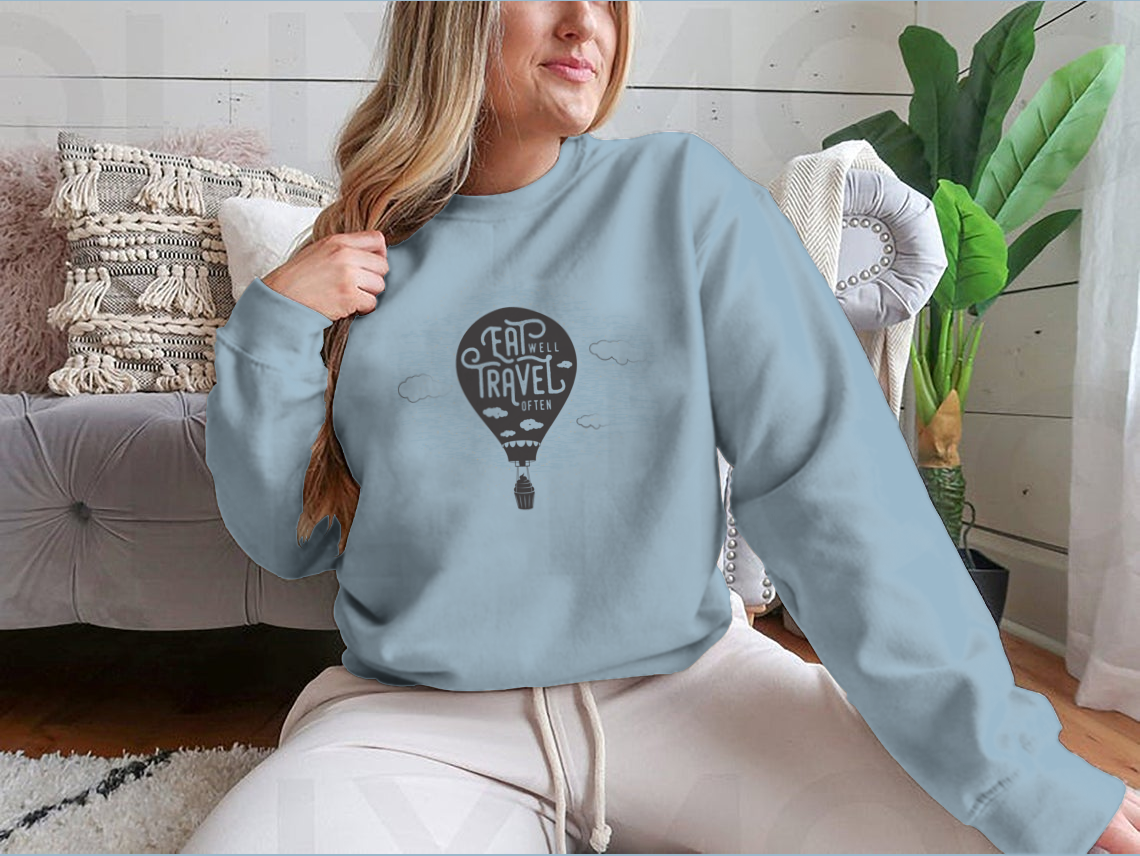 A cozy sweatshirt featuring a cute design of a cupcake riding towards colorful balloons in a bright sky with clouds.