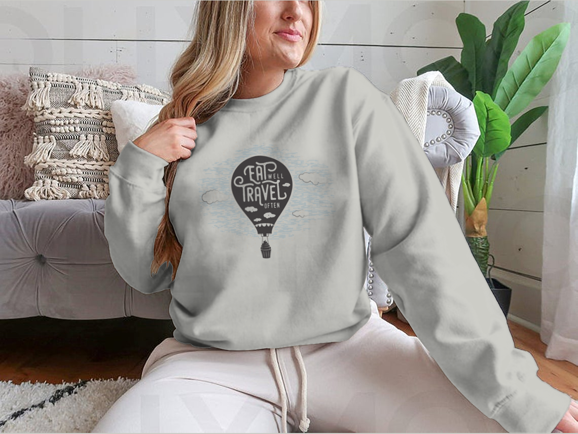 A cozy sweatshirt featuring a cute design of a cupcake riding towards colorful balloons in a bright sky with clouds.