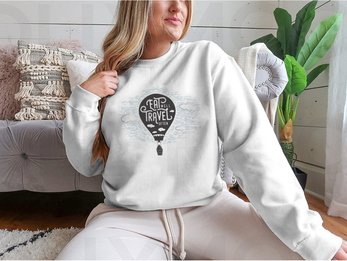 A cozy sweatshirt featuring a cute design of a cupcake riding towards colorful balloons in a bright sky with clouds.