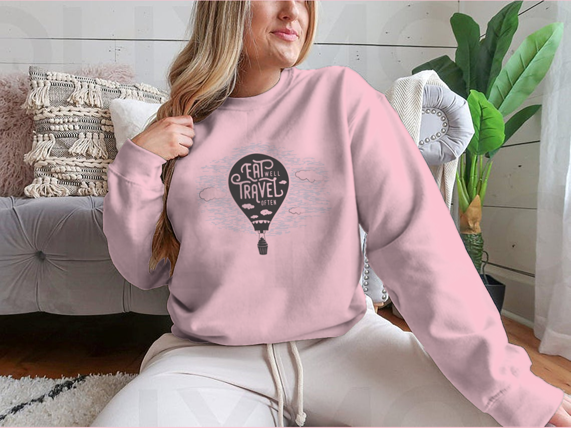 A cozy sweatshirt featuring a cute design of a cupcake riding towards colorful balloons in a bright sky with clouds.