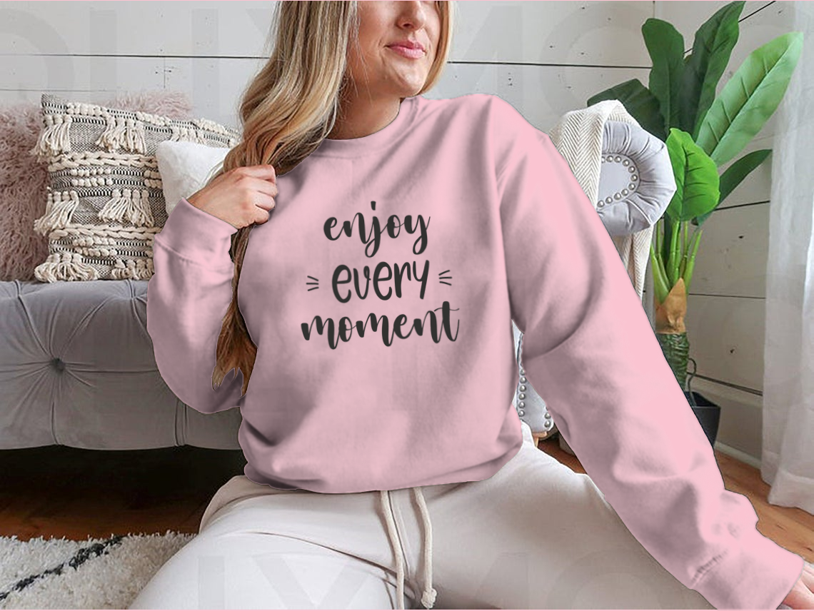 A cozy sweatshirt featuring brush lettering design that reads 'Enjoy Every Moment', made from soft cotton fabric.