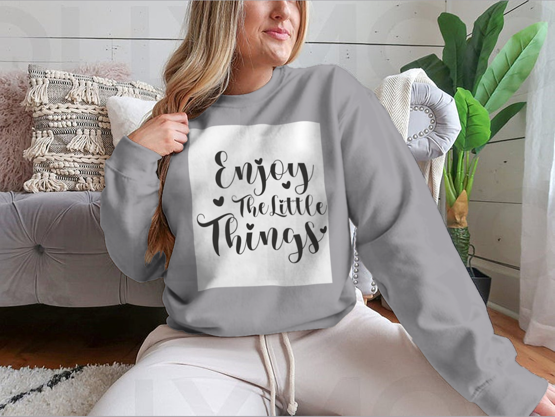 A cozy sweatshirt featuring the calligraphy design 'Enjoy The Little Things', showcasing its soft fabric and classic fit.