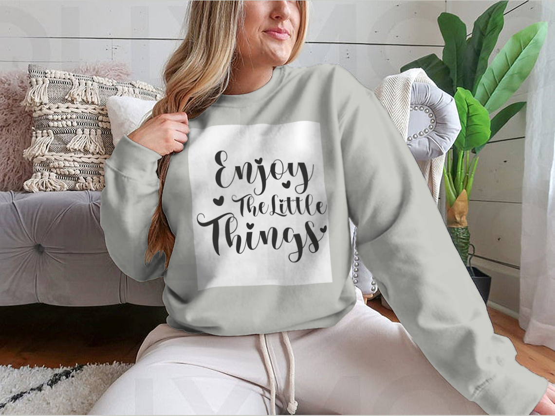 A cozy sweatshirt featuring the calligraphy design 'Enjoy The Little Things', showcasing its soft fabric and classic fit.