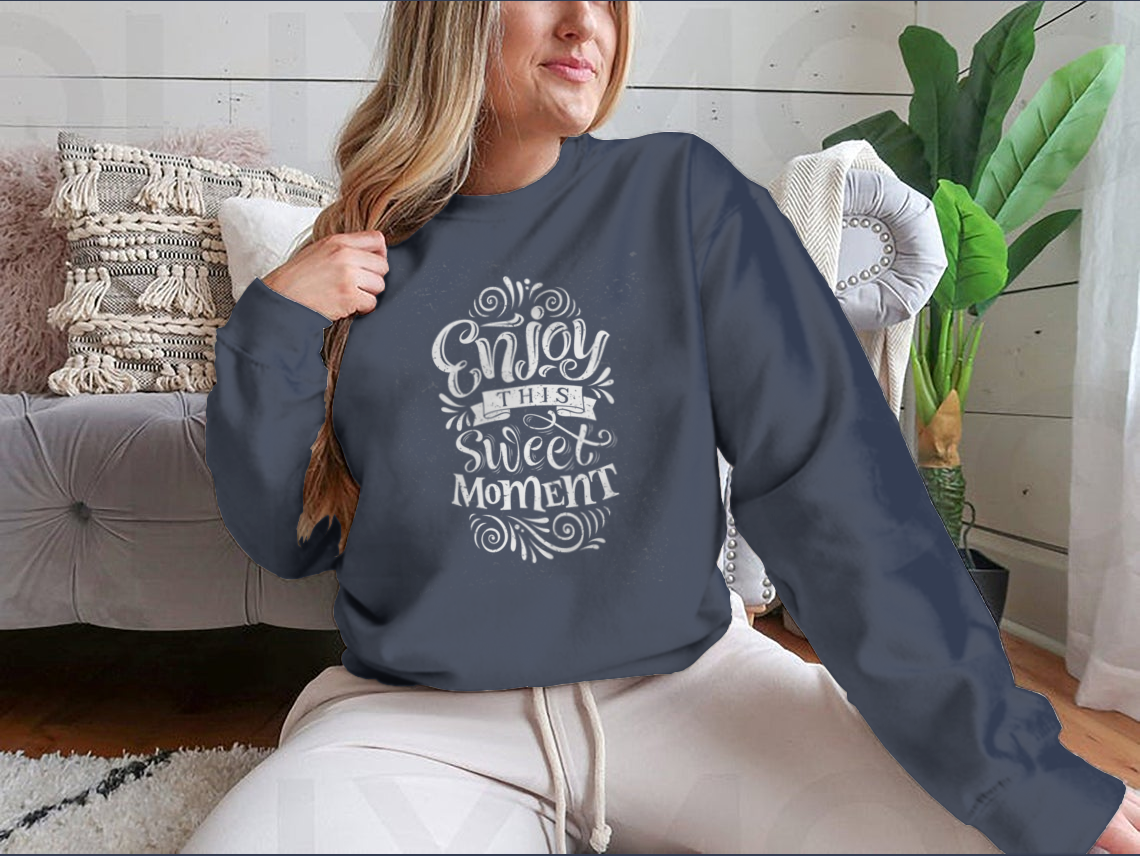 A cozy sweatshirt featuring the phrase 'Enjoy This Sweet Moment' in stylish typography, made from a soft cotton/polyester blend.