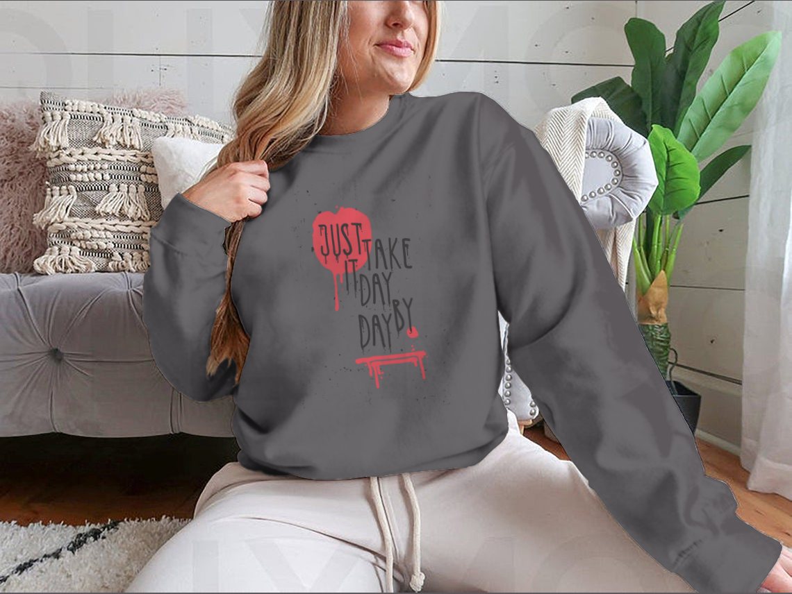 A cozy sweatshirt featuring the motivational phrase 'Just Take It Day By Day' in stylish typography, perfect for casual wear.