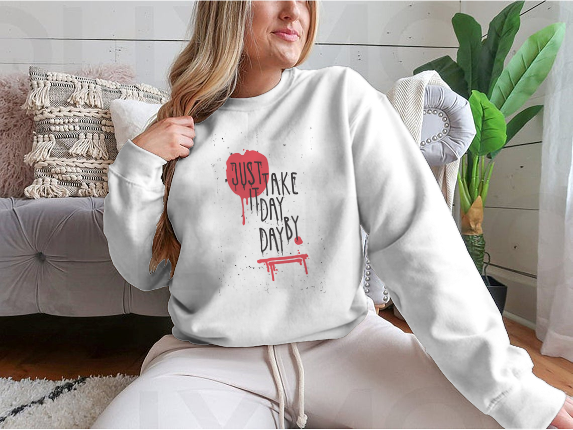 A cozy sweatshirt featuring the motivational phrase 'Just Take It Day By Day' in stylish typography, perfect for casual wear.