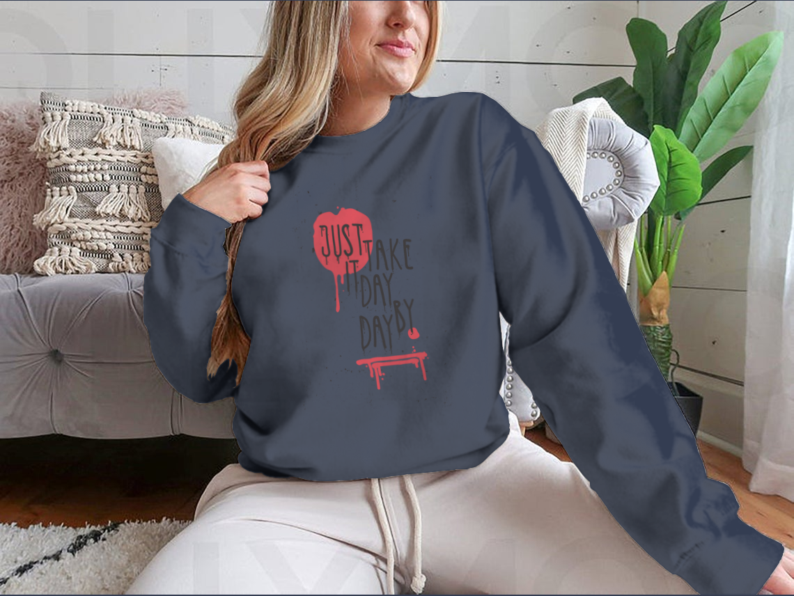 A cozy sweatshirt featuring the motivational phrase 'Just Take It Day By Day' in stylish typography, perfect for casual wear.