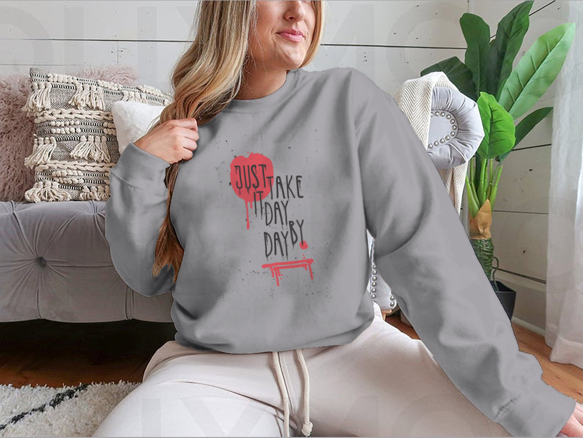 A cozy sweatshirt featuring the motivational phrase 'Just Take It Day By Day' in stylish typography, perfect for casual wear.