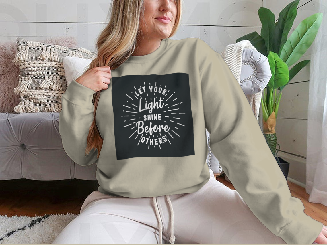 A stylish hand lettering typography shirt with the phrase 'Let Your Light Shine Before Others' displayed prominently, made from soft cotton fabric.