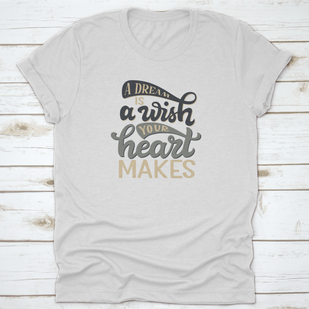 A stylish t-shirt featuring the hand-drawn quote 'A Dream Is A Wish Your Heart Makes' in elegant typography, made from soft cotton fabric.