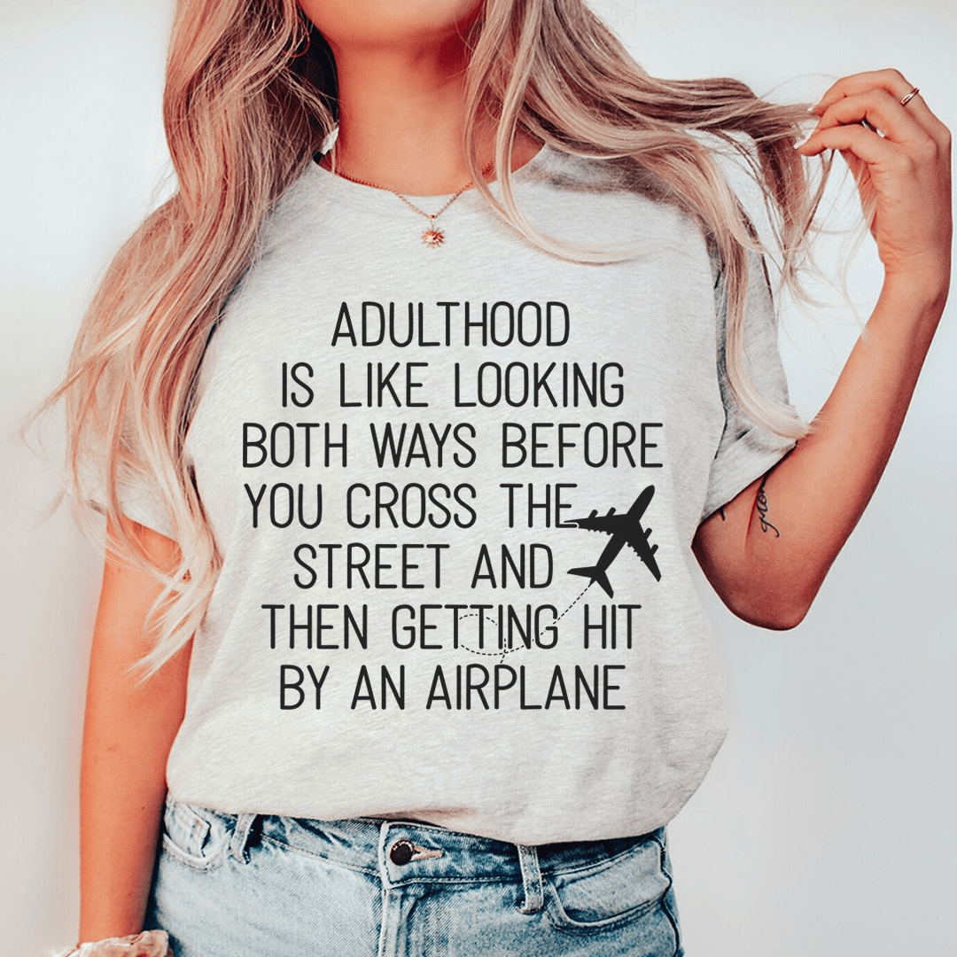 A humorous t-shirt with the phrase 'Adulthood Is Like Looking Both Ways Before You Cross The Street' printed on it, made from soft cotton.