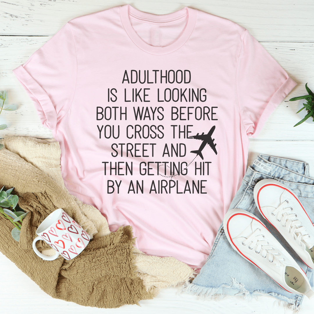 A humorous t-shirt with the phrase 'Adulthood Is Like Looking Both Ways Before You Cross The Street' printed on it, made from soft cotton.