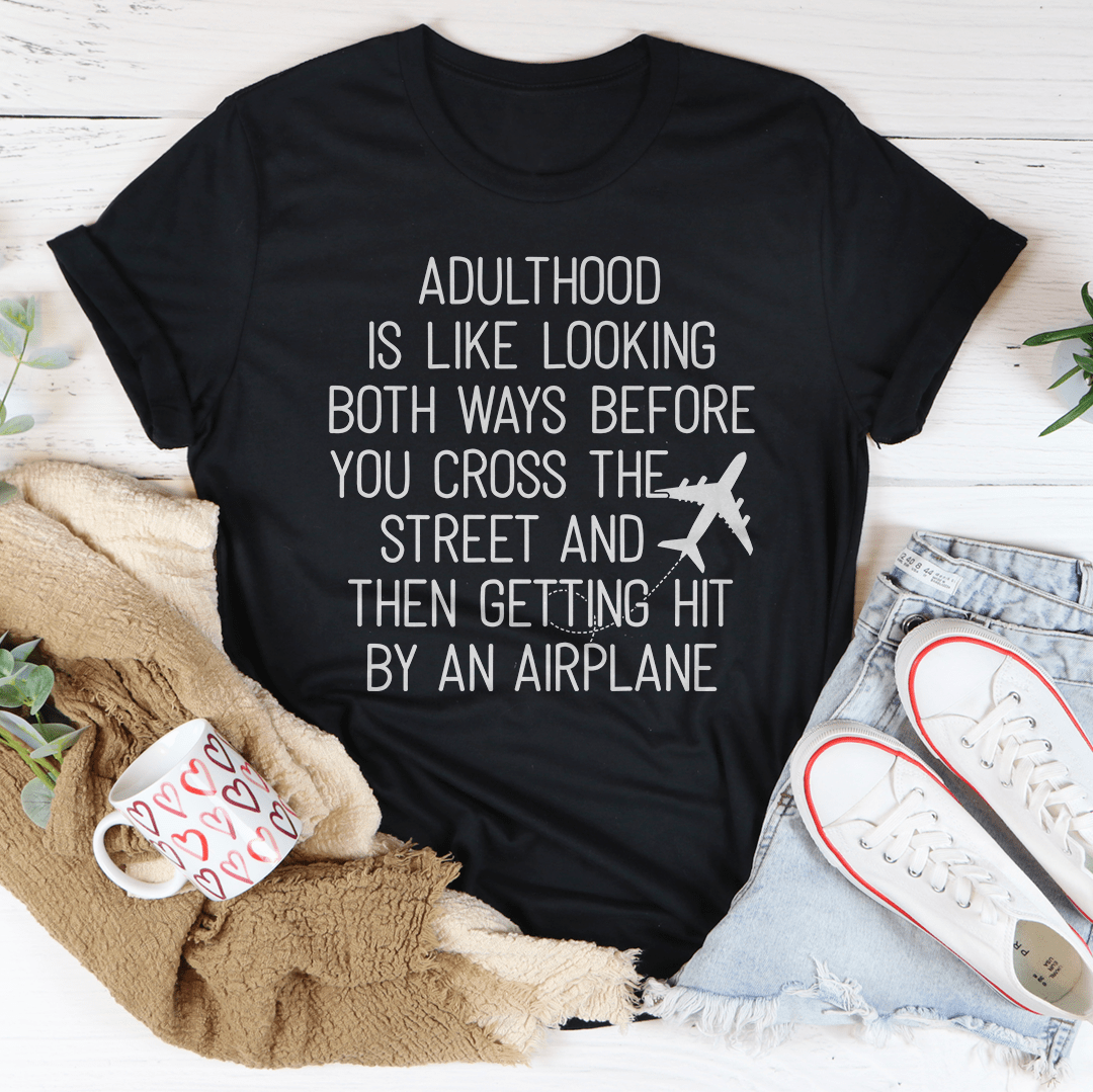 A humorous t-shirt with the phrase 'Adulthood Is Like Looking Both Ways Before You Cross The Street' printed on it, made from soft cotton.