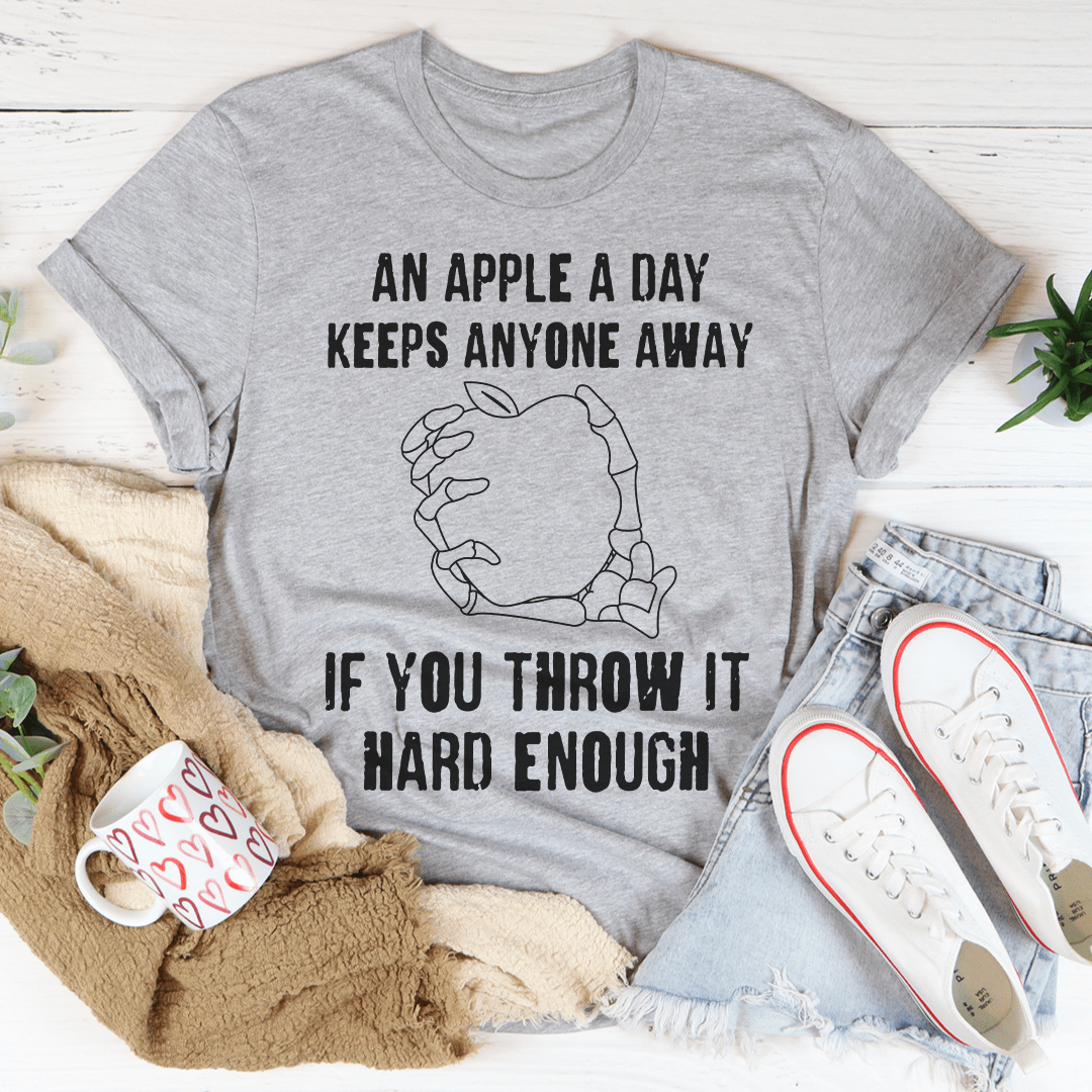 A humorous t-shirt featuring the phrase 'An Apple A Day Keeps Anyone Away If You Throw It Hard Enough', made from soft cotton.