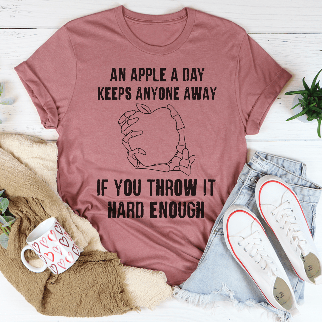 A humorous t-shirt featuring the phrase 'An Apple A Day Keeps Anyone Away If You Throw It Hard Enough', made from soft cotton.