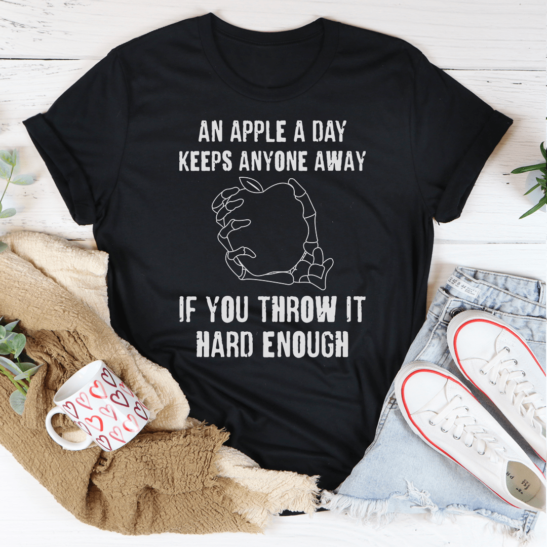 A humorous t-shirt featuring the phrase 'An Apple A Day Keeps Anyone Away If You Throw It Hard Enough', made from soft cotton.