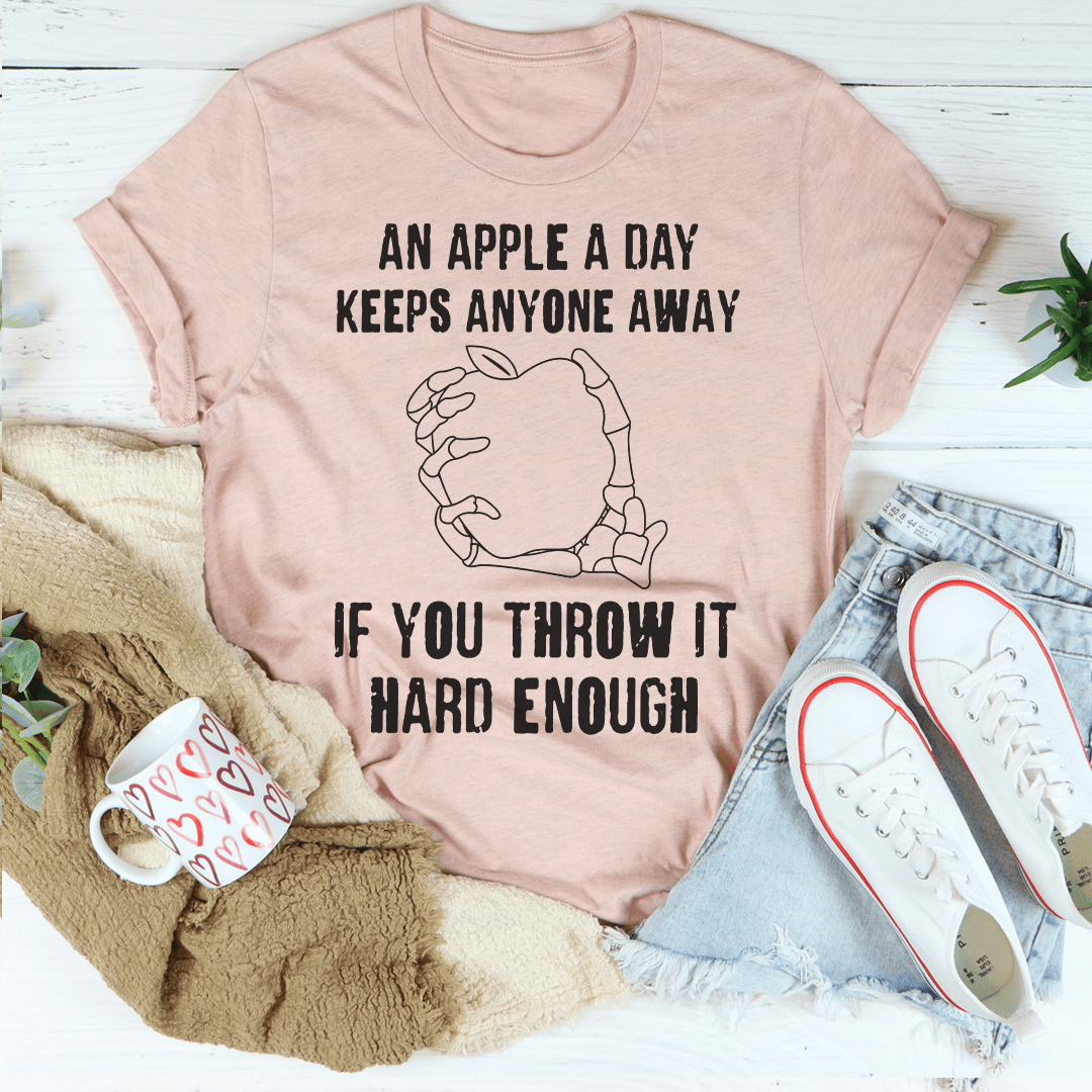 A humorous t-shirt featuring the phrase 'An Apple A Day Keeps Anyone Away If You Throw It Hard Enough', made from soft cotton.