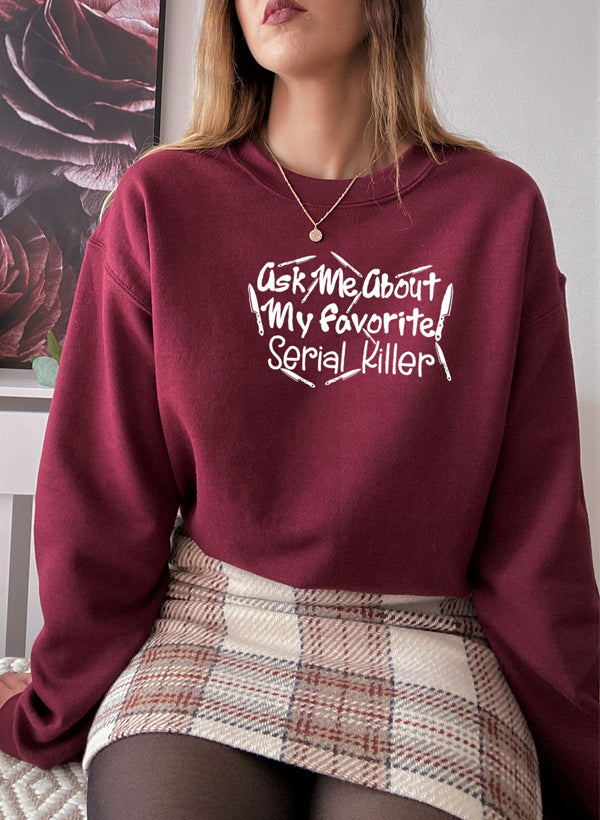 A cozy black sweatshirt featuring the phrase 'Ask Me About My Favorite Serial Killer' in bold white letters, perfect for casual wear.