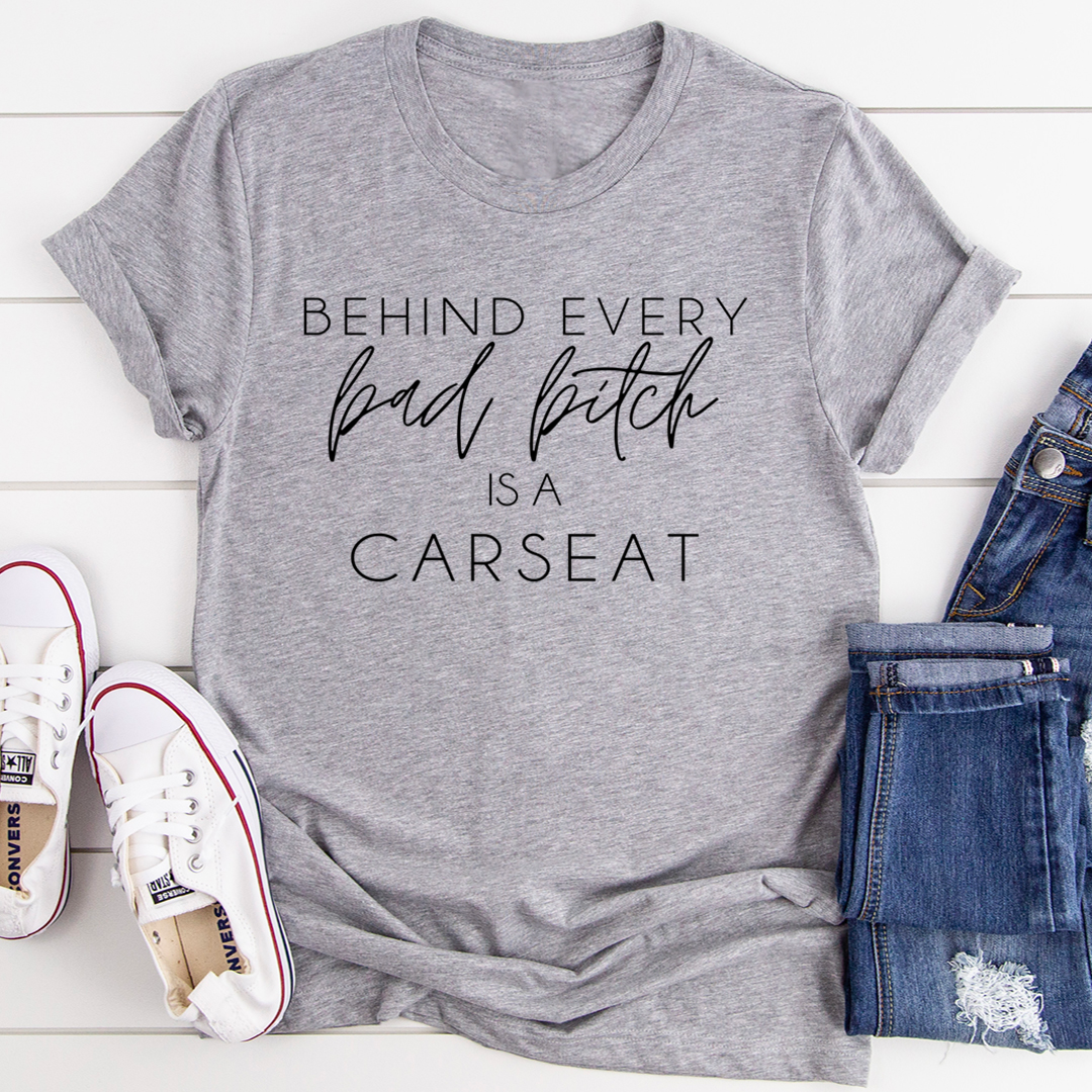 A stylish t-shirt featuring the phrase 'Behind Every Bad B Is A Car Seat', made from soft ring-spun cotton with double stitching.