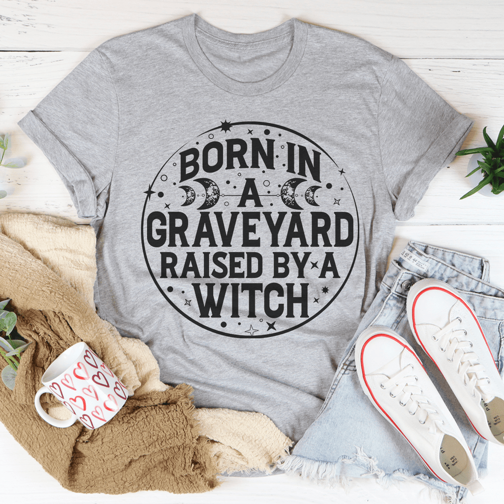 Born In A Graveyard Raised By A Witch T-Shirt displayed on a mannequin, showcasing its unique design and soft fabric.