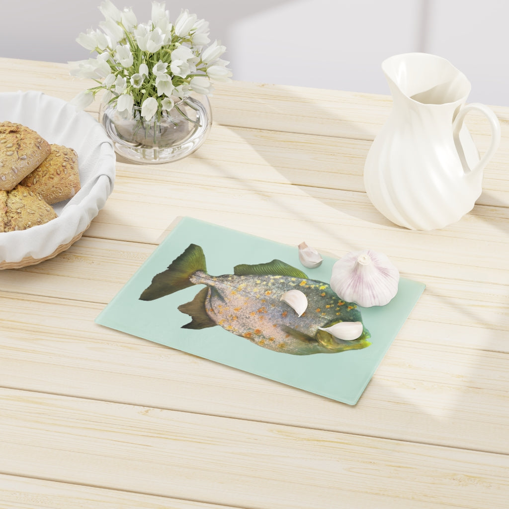 A stylish Fish with Specs Cutting Board made of tempered glass, featuring a unique fish design and four rubber dots for stability.