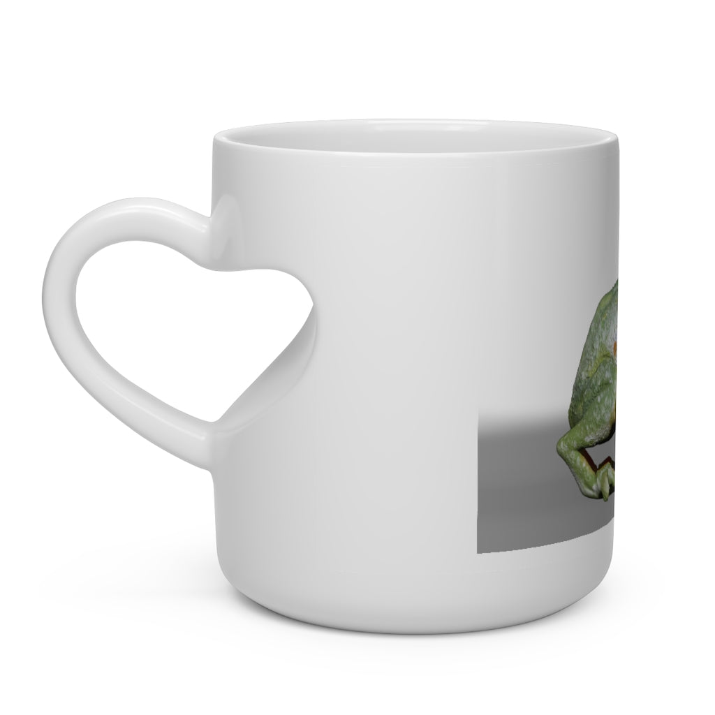 A white ceramic mug shaped like a heart with a frog design, featuring a heart-shaped handle, perfect for hot beverages.