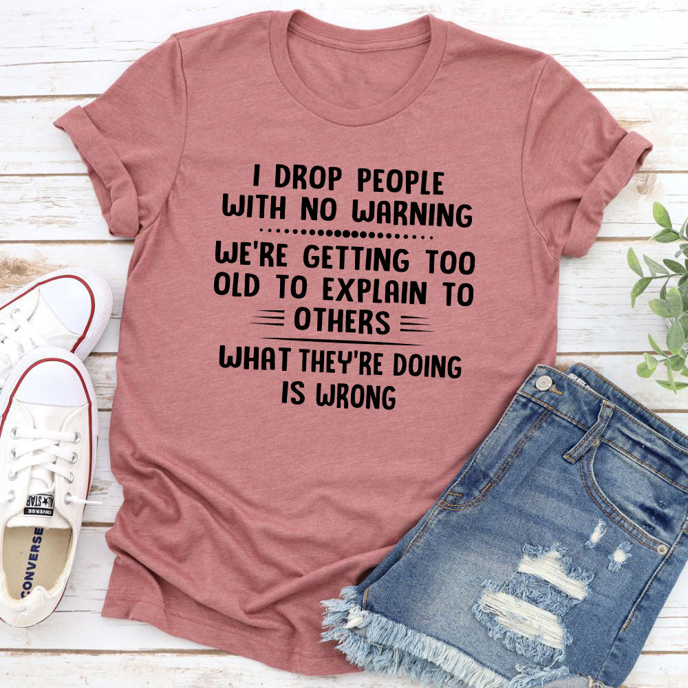 I Drop People With No Warning T-Shirt featuring bold text on a soft cotton fabric, showcasing its durability and comfort.