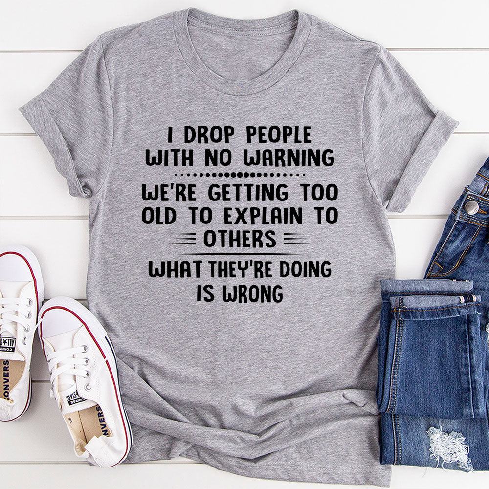 I Drop People With No Warning T-Shirt featuring bold text on a soft cotton fabric, showcasing its durability and comfort.