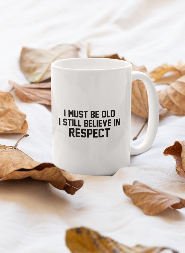 A stylish 11oz ceramic mug with a glossy finish featuring the phrase 'I Must Be Old I Still Believe In Respect' in bold lettering.