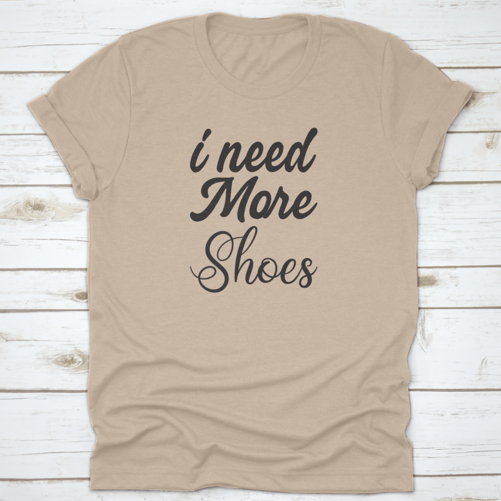 A stylish grey T-shirt featuring the quote 'I Need More Shoes' in bold letters, made from soft cotton fabric.